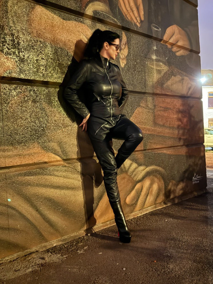 Woman in black leather outfit posing against a mural.