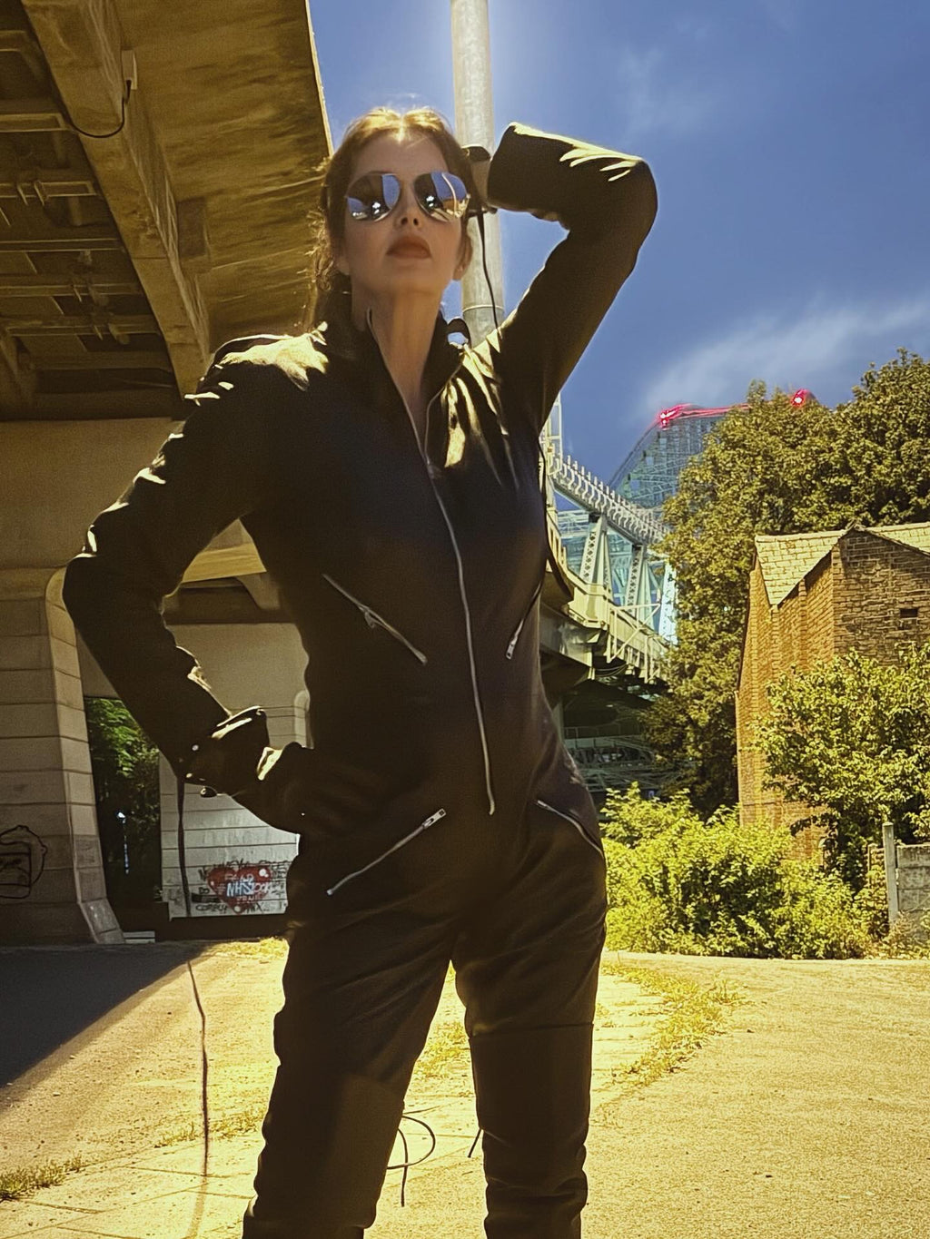 Person in a dark outfit with sunglasses standing outdoors under a clear blue sky.
