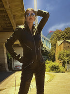 Person in a dark outfit with sunglasses standing outdoors under a clear blue sky.
